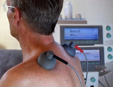 Somministrazione elettroterapia alla spalla a paziente maschio con gli occhiali